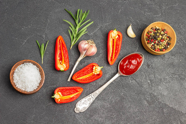 Allspice and salt in wooden bowls. Raw red pepper, garlic and tomato sauce in spoon. Copy space. Flat lay. Black background - Photo, image