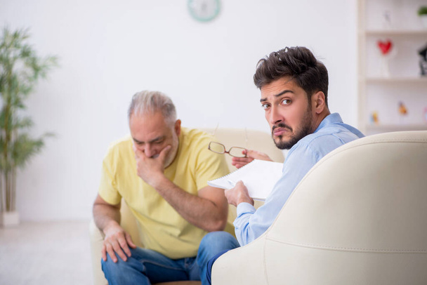 Viejo visitando joven psicoterapeuta masculino - Foto, Imagen