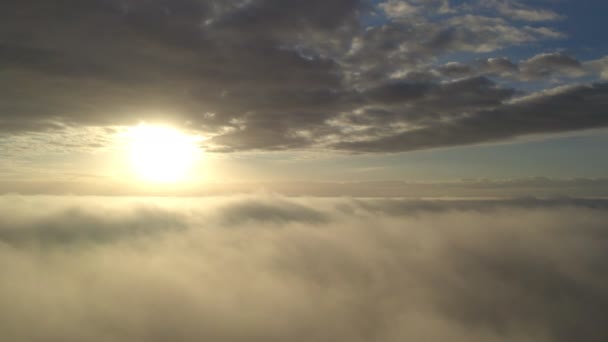 Вид с воздуха. Летит в тумане, летит в тумане над утренними облаками под восходящим солнцем. Снимок с воздуха. Лети над облаками к солнцу с проплывающими туманами. Туманная погода - Кадры, видео
