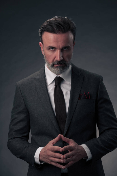 Porträt eines erfolgreichen eleganten Geschäftsmannes mit grauem Bart und lässiger Businesskleidung in einem Fotostudio, isoliert auf dunklem Hintergrund, gestikulierend mit den Händen. Hochwertiges Foto - Foto, Bild