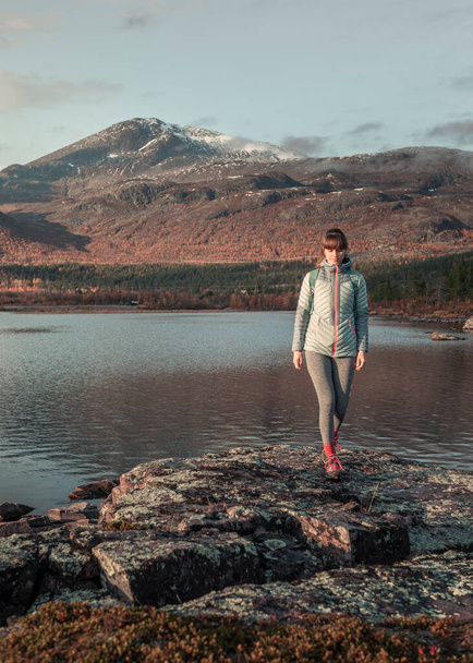 Woman walking in mountain landscape with lake and rocks in Stora Sjoefallet National Park in autumn in Lapland in Sweden from above during sunset - Zdjęcie, obraz