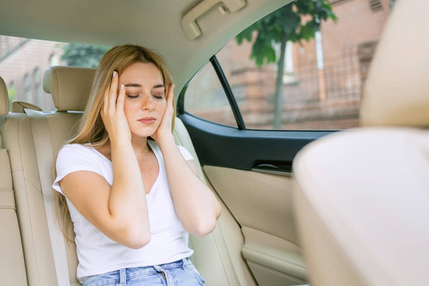 Une jeune femme fatiguée souffrant de migraine est assise sur le siège arrière d'un véhicule - Photo, image
