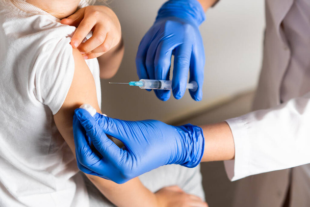 вакцинация детей, маленькая девочка на приеме у врача, инъекция в руку, рожок, крупный план - Фото, изображение
