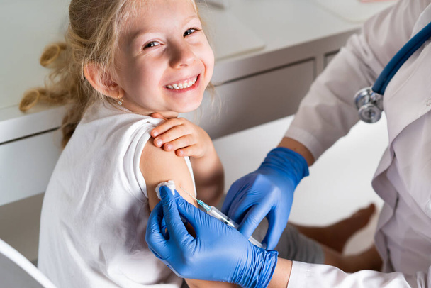 vaccination of children, a little girl at a doctors appointment, an injection in the arm, the conce - Fotografie, Obrázek