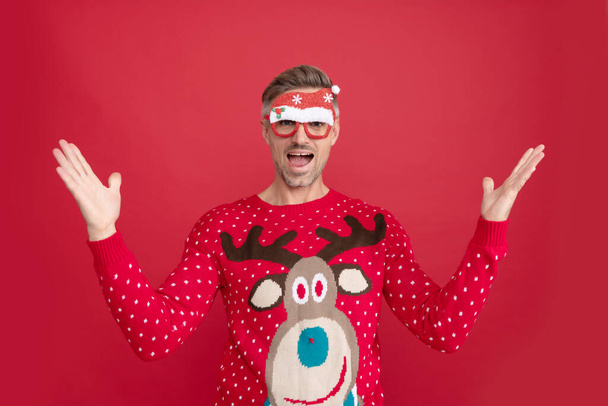 amazed man in winter sweater and party santa claus glasses. xmas guy - Foto, afbeelding