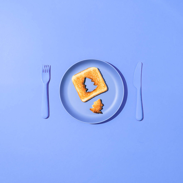 Toasted bread with a slice in the shape of a christmas tree on a blue plate. Minimal holiday flat lay concept. - Fotografie, Obrázek