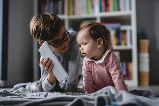 Ağabeyi dijital tablet erkek ve kız kardeş çocukluğu kavramını gösterirken küçük beyaz bir kız bebek evde yerde sürünüyor. - Fotoğraf, Görsel