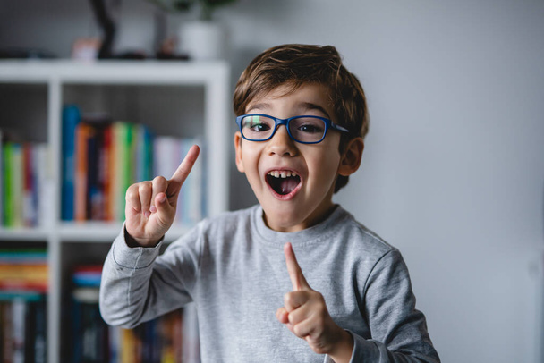 One small happy caucasian boy close up looking to the camera while standing at home wearing eyeglasses and making fun faces and gesture real people copy space happiness and joy childhood concept - Valokuva, kuva