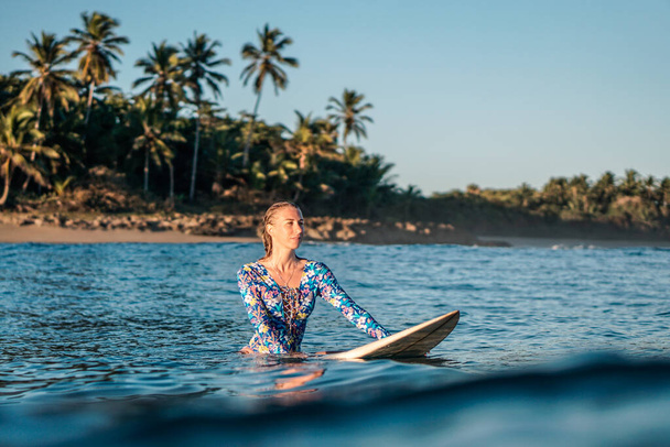 Portrait of blond surfer girl on white surf board in blue ocean pictured from the water in Encuentro beach in Dominican Republic - Zdjęcie, obraz