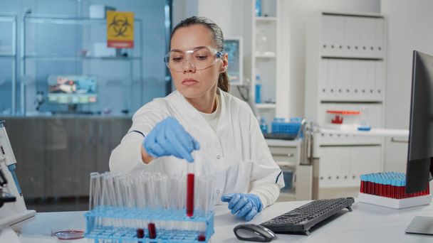Microbiólogo analizando tubo de ensayo con sustancia roja en laboratorio científico - Foto, imagen