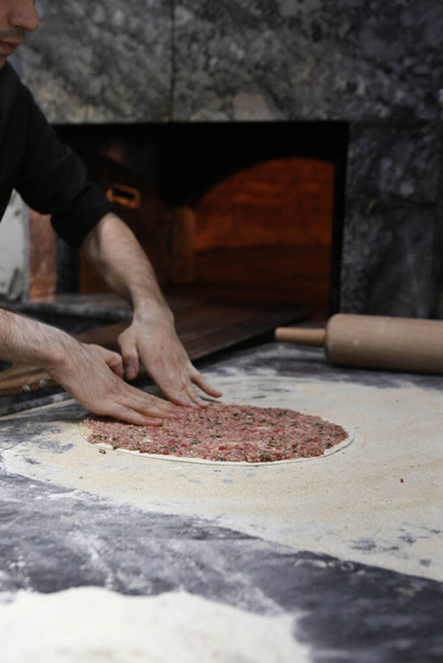 Török pizza vagy lahmacun készítése - gyorsétterem és népszerű utcai ételek a mediterrán országokban. Tészta, darált hús és növényi összetevők a török pide főzéséhez. - Fotó, kép