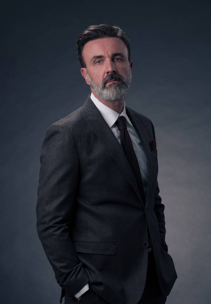 Portrait of a successful stylish elegant senior businessman with a grey beard and casual business clothes confident in photo studio isolated on dark background gesturing with hands. High-quality photo - Foto, Imagem