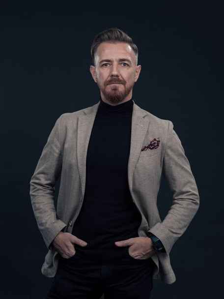 Portrait of a successful stylish elegant senior businessman with a grey beard and casual business clothes confident in photo studio isolated on dark background gesturing with hands. High-quality photo - Foto, Bild