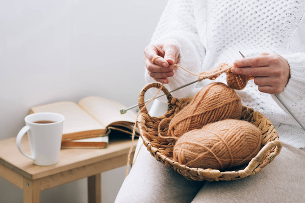 Une femme d'âge moyen est engagée dans le tricot artisanal à la maison, tricotant avec des fils. Loisirs à domicile pendant le temps libre - Photo, image