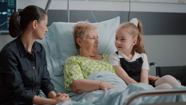 Племянница и больная бабушка обнимаются во время семейного визита в палату больницы - Фото, изображение