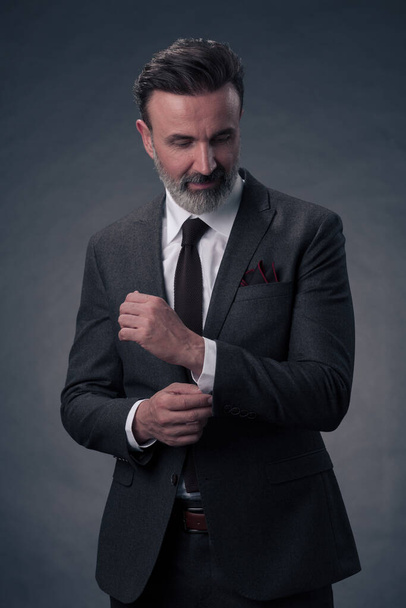 Portrait of a successful stylish elegant senior businessman with a grey beard and casual business clothes confident in photo studio isolated on dark background gesturing with hands. High-quality photo - Foto, imagen