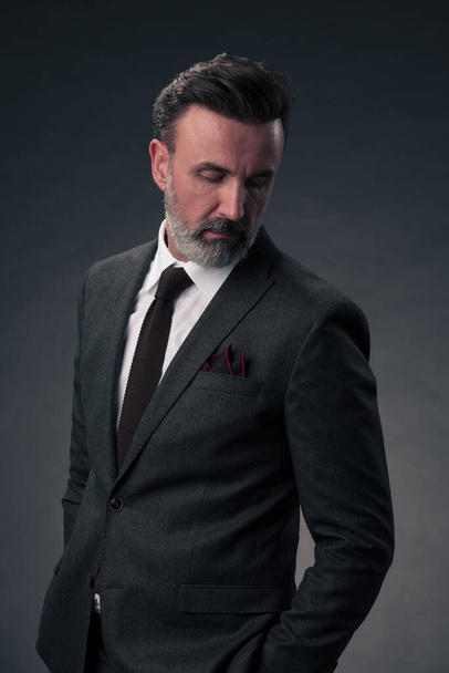 Portrait of a successful stylish elegant senior businessman with a grey beard and casual business clothes confident in photo studio isolated on dark background gesturing with hands. High-quality photo - Foto, afbeelding