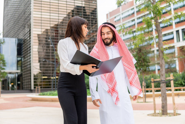 Young european female assistant showing contract document to arab businessman on city street - Photo, Image