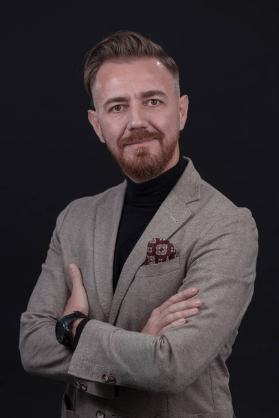 Portrait of a stylish elegant senior businessman with a beard and casual business clothes in photo studio isolated on dark background gesturing with hands. High quality photo - Foto, imagen