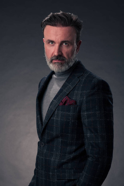 Portrait of a successful stylish elegant senior businessman with a grey beard and casual business clothes confident in photo studio isolated on dark background gesturing with hands. High-quality photo - Foto, imagen