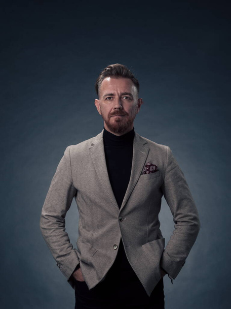 Portrait of a successful stylish elegant senior businessman with a grey beard and casual business clothes confident in photo studio isolated on dark background gesturing with hands. High-quality photo - Foto, immagini