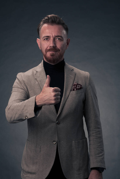 Portrait of a successful stylish elegant senior businessman with a grey beard and casual business clothes confident in photo studio isolated on dark background gesturing with hands. High-quality photo - Foto, Imagem