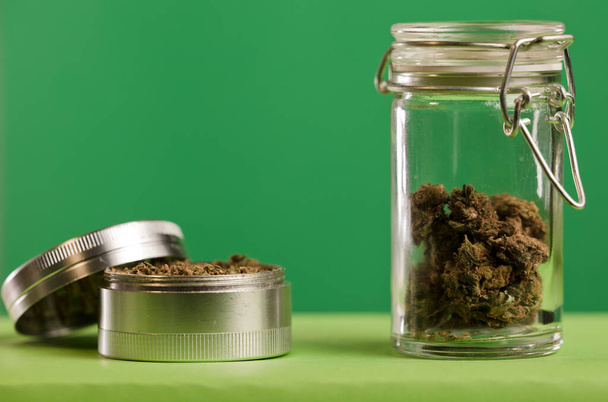 marijuana sul macinino, vasi di vetro sul tavolo, con sfondo verde scuro. - Foto, immagini
