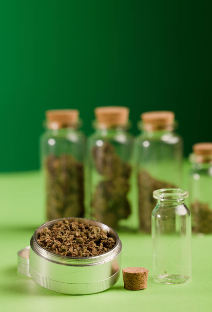 maconha picada em um moedor, e jarros de vidro hermético com diferentes tipos de cannabis e livros verdes, um processo para a produção de maconha pura. fundo verde - Foto, Imagem
