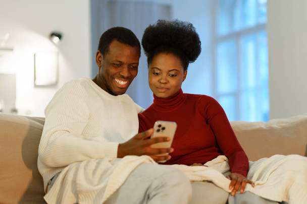 Χαμογελώντας νεαρό ζευγάρι από την Αφρική στο σπίτι κάνοντας βιντεοσκόπηση στο smartphone, κουβεντιάζοντας online - Φωτογραφία, εικόνα