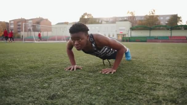 Młoda czarna dziewczyna trening na stadionie miasta i robi push up na sztucznej nawierzchni boiska do piłki nożnej - Materiał filmowy, wideo