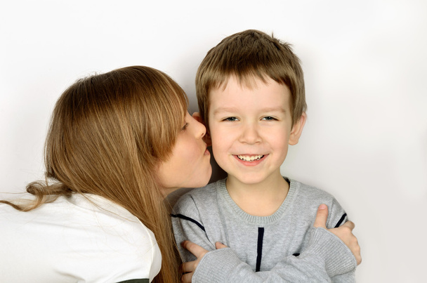 дівчина цілує маленького веселого хлопчика на світло-сірому фоні. він пішов
 - Фото, зображення