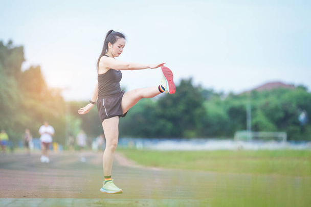 Egy érett gyönyörű ázsiai nő sport ruhák nyújtózkodik edzés előtt szabadtéri a városi stadion parkban reggel, hogy egy egészséges életmódot. Egészséges fiatal nő melegszik a szabadban - Fotó, kép