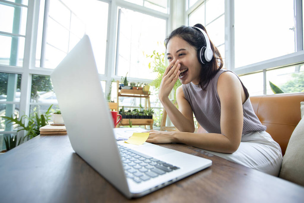 Ázsiai üzletasszonyok használ notebook számítógépek és visel fülhallgatót az online találkozók és a munka otthonról. - Fotó, kép