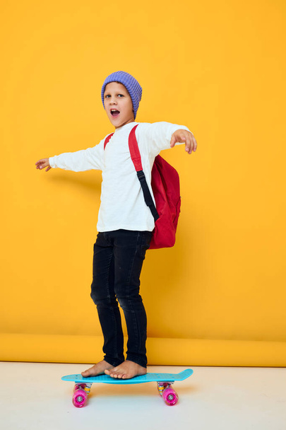 portrait of cute boys with red backpack blue skateboard yellow color background - 写真・画像