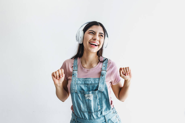 Portrait of latin young smiling woman with headphones, dancing and listening to music on a white background in Latin America - Fotografie, Obrázek