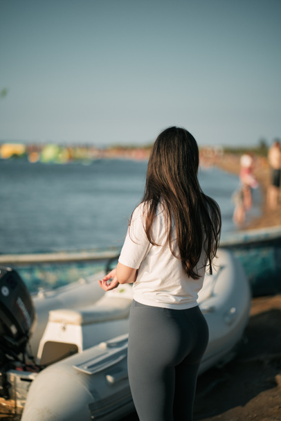 Sportieve vrouw aan de kust met een wit shirt en legging. Gekleed fitness vrouw op het strand. - Foto, afbeelding