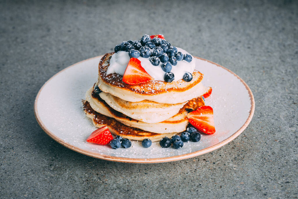 A vertical shot of a plate with gourmet pancakes with cream, strawberries, and blueberries - Foto, Bild