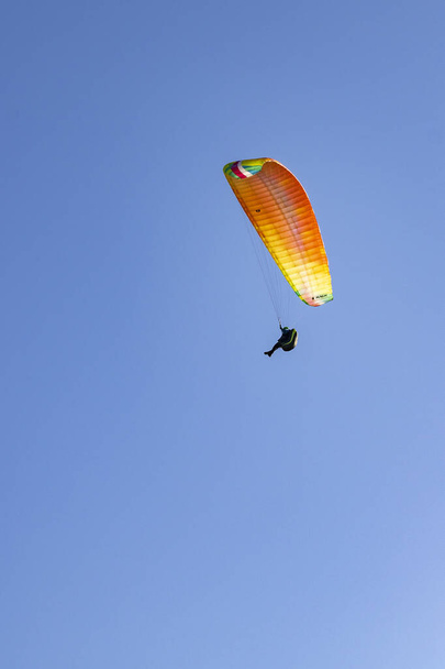Un disparo vertical de un parapente volando en un colorido paracaídas contra un cielo azul claro - Foto, imagen
