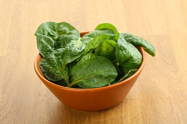 Свежие зеленые листья шпината в миске на деревянном фоне - Фото, изображение