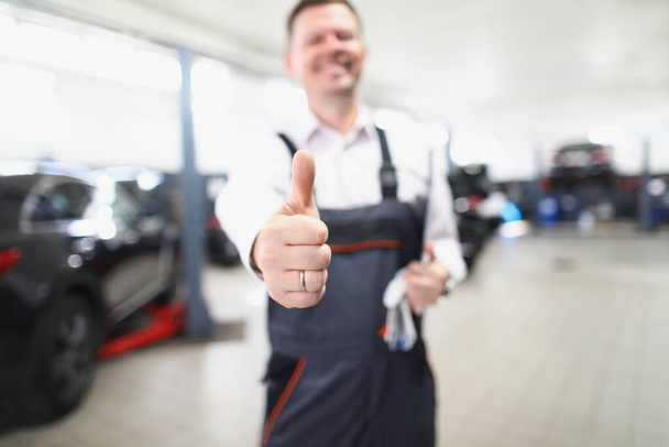 Працівник служби обслуговування автомобілів показує великі пальці вгору і щасливо посміхається
 - Фото, зображення