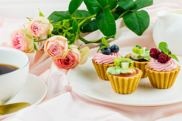 romantic composition for Valentine's Day, holiday, birthday. mini tartlets with cream and fruits on a plate, a cup of coffee, a bouquet of roses - Fotó, kép