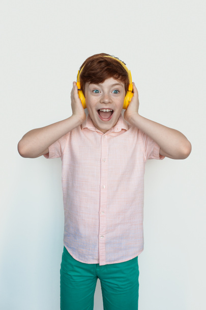 Niño caucásico sorprendido escuchando música en auriculares sobre fondo blanco - Foto, imagen