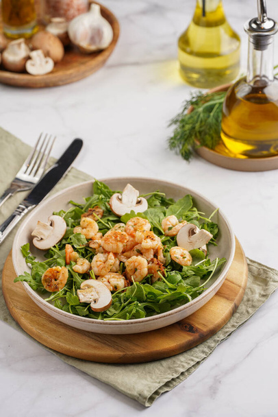 Arugula salad with shrimp and champignons, olive oil and dill on a wooden board on a white surface - Zdjęcie, obraz