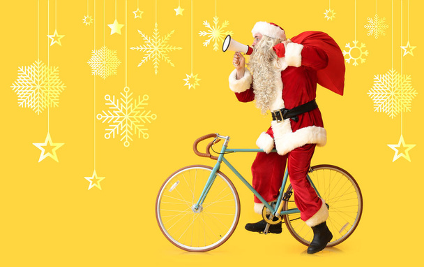 Santa Claus with megaphone, bag and bicycle on yellow background - Photo, Image