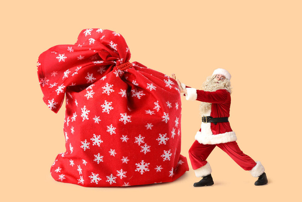 Santa Claus near big bag full on gifts on color background - Photo, Image