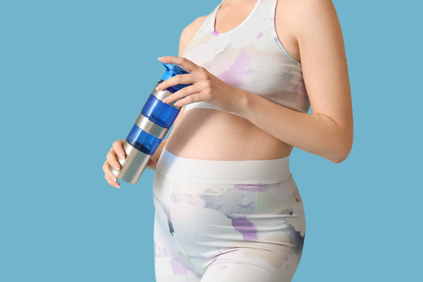 Jovem mulher grávida abertura garrafa de água no fundo azul - Foto, Imagem
