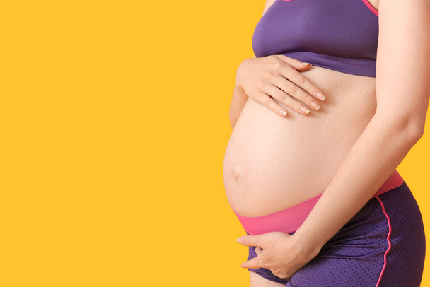 Jeune femme enceinte sportive sur fond jaune - Photo, image