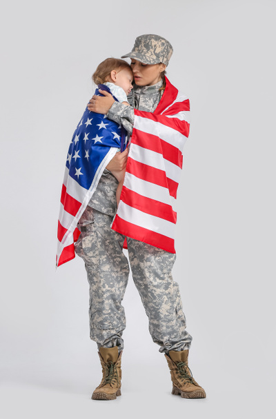 Female soldier and her little daughter with USA flag on light background - 写真・画像