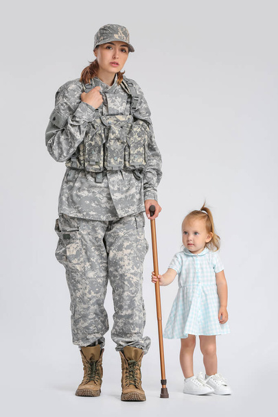 Γυναίκα στρατιώτης με μπαστούνι και η κόρη της στο φως φόντο - Φωτογραφία, εικόνα