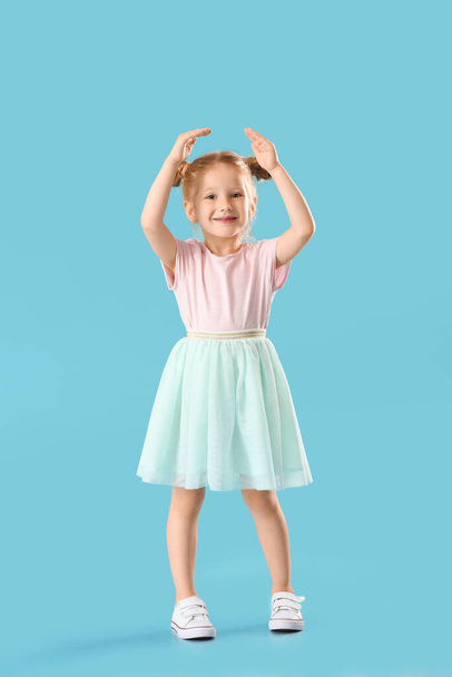 schattig klein meisje in rok dansen op blauwe achtergrond - Foto, afbeelding